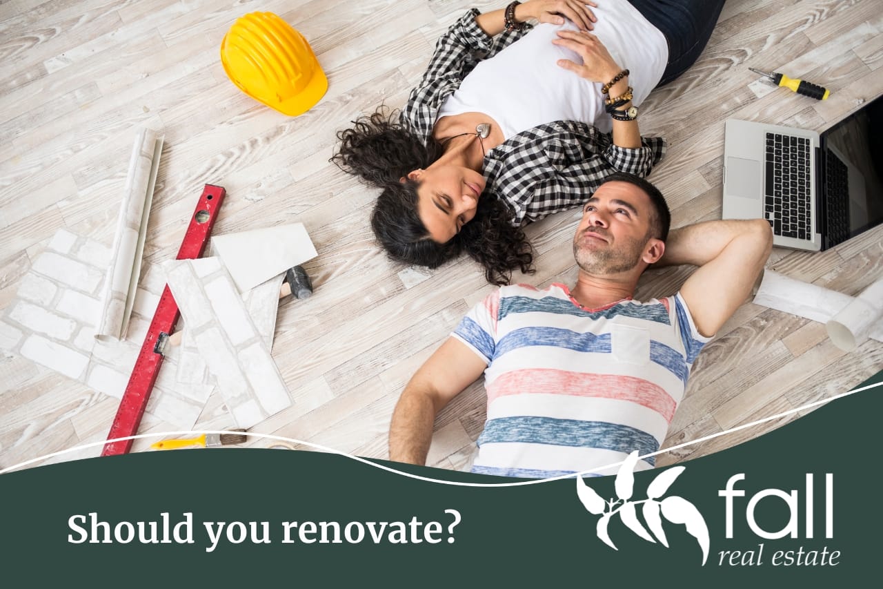 A couple laying on the floor with tools surrounding them contemplating whether they should renovate or not before selling.